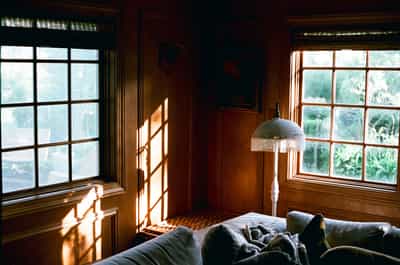 Beautiful family room bathed in golden hour sunlight streaming through large windows, creating dramatic light patterns across wood paneling and comfortable seating, captured on Aerocolor IV film