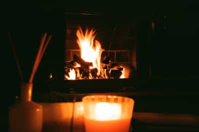 Intimate evening scene featuring a crackling fireplace with dancing flames and glowing candles creating warm ambient light in cozy family room, shot on ColorPlus 200 film